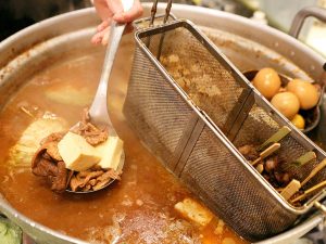 大鍋の中で煮込まれたモツや豆腐。串物が浸かったザルの向こうには煮卵も