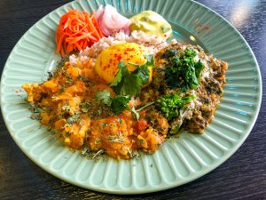 左下が、新玉トマトチキンカレー、右が菜の花とほうれん草のチキンカレー、真ん中がスパイス味玉、上には、副菜のスパイスキャロットラペ、新玉ねぎのアチャール、アスパラガスのライタ