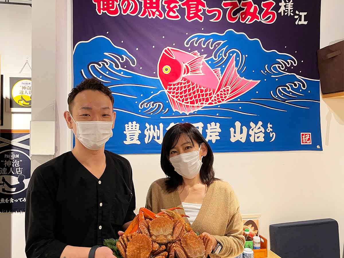 『俺の魚を食ってみろ！！』西新宿店・店長の石井圭一郎さん（左）と、株式会社AO代表取締役・前原妙子さん。現在実施中の8000円で食べ放題のカニを持って