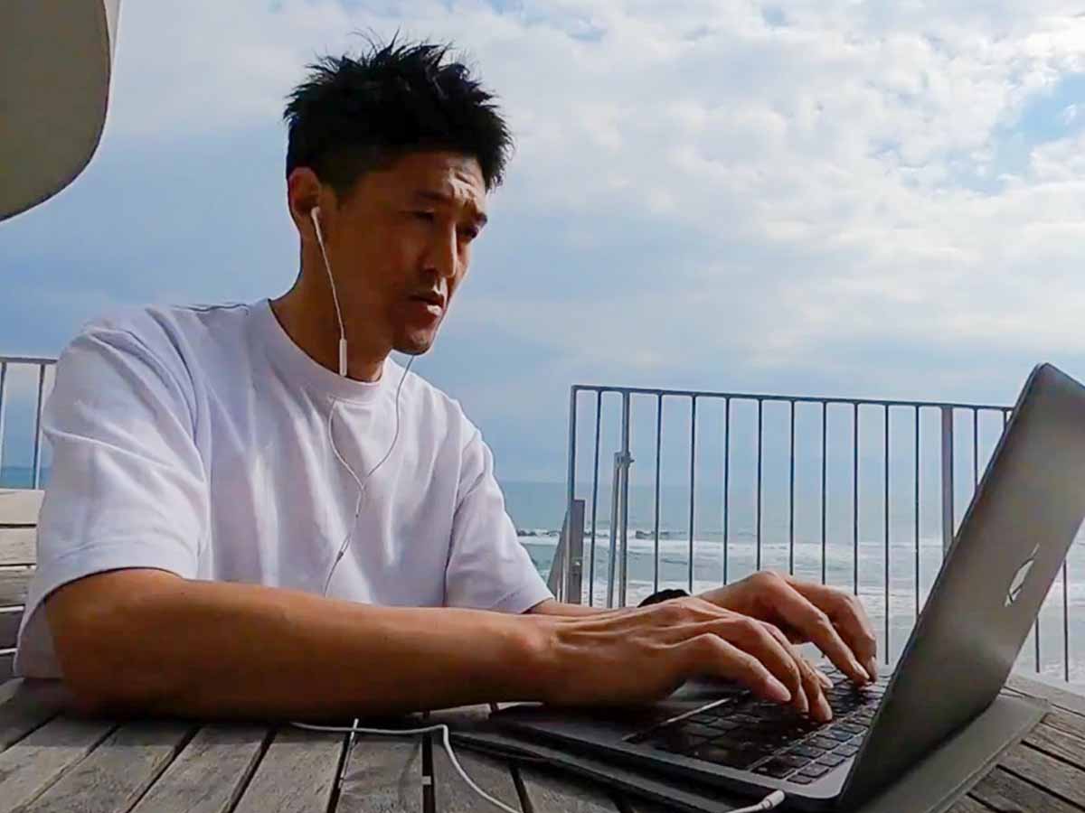 宮崎県日向市に滞在時のワーケーションおじさん。海をバックに、ノートパソコンを開いてメールチェック