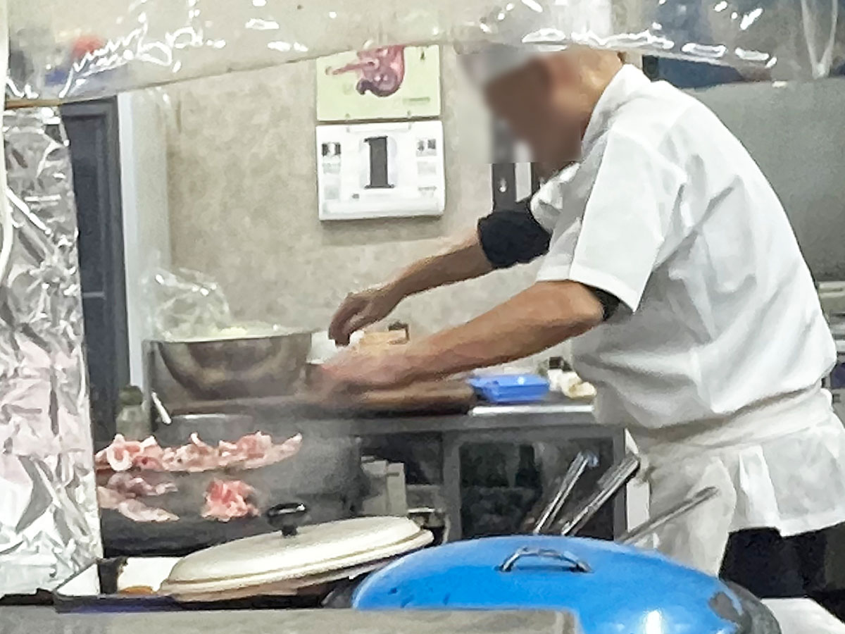 厨房の鉄板で手際よく豚バラ肉を焼く店員さん