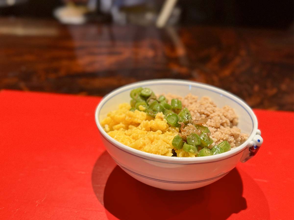 「鶏そぼろ三食丼」には2種類のカンロ飴が使われ、インゲンにはかつおぶし、具材とごはんの間には昆布を重ねて隠し味に。彩りも鮮やか！ ［食楽web］