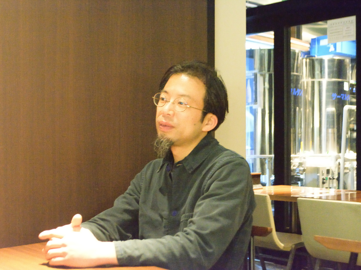 感心しながら松枝さんの話を聞く佐藤さん。後ろに見えるのが6畳にも満たない店内の醸造所