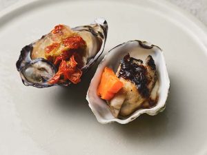 同じ食材への異なるアプローチが興味を引く一皿。松石シェフ（右）は豆鼓をあわせた中華風、寺田シェフ（左）は低温調理で生牡蠣のような味わいを演出