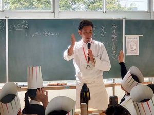 木嶋隆文氏（TERAKOYA）による「味覚の授業」の様子。持参のコンソメの旨味が、多くの食材と時間によって作られていることを説明。（2024年、学芸大学附属小金井小学校にて）