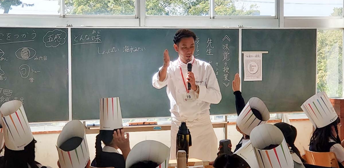 木嶋隆文氏(TERAKOYA)による「味覚の授業」の様子。持参のコンソメの旨味が、多くの食材と時間によって作られていることを説明。(2024年、学芸大学附属小金井小学校にて)
