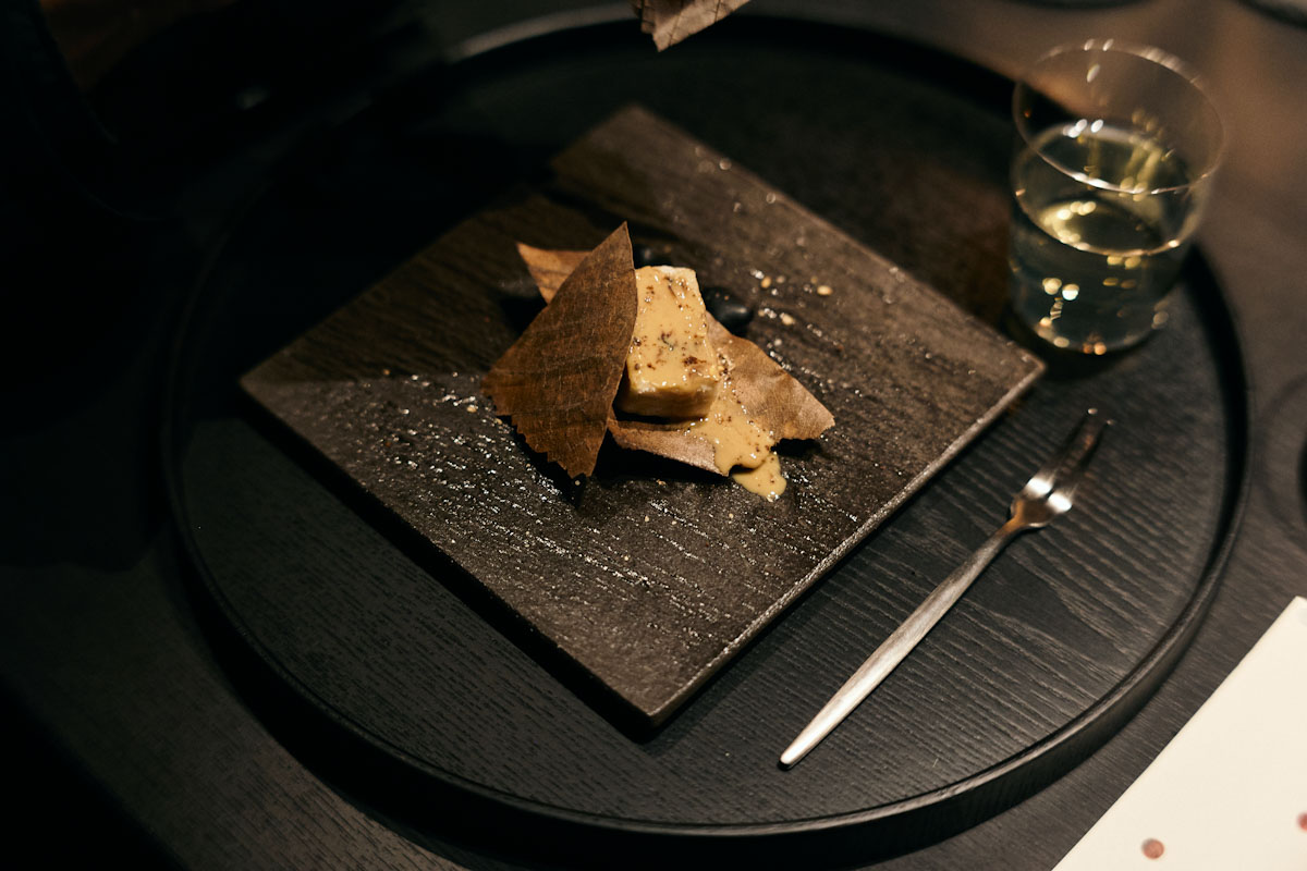 「聴く」テーマにした一皿。炭火の香りをまとったごま豆腐。皿の下に敷かれた玉砂利が擦れ合う音は、余市蒸溜所で守り続けられてきた石炭直火蒸溜の音と重なります[食楽web]